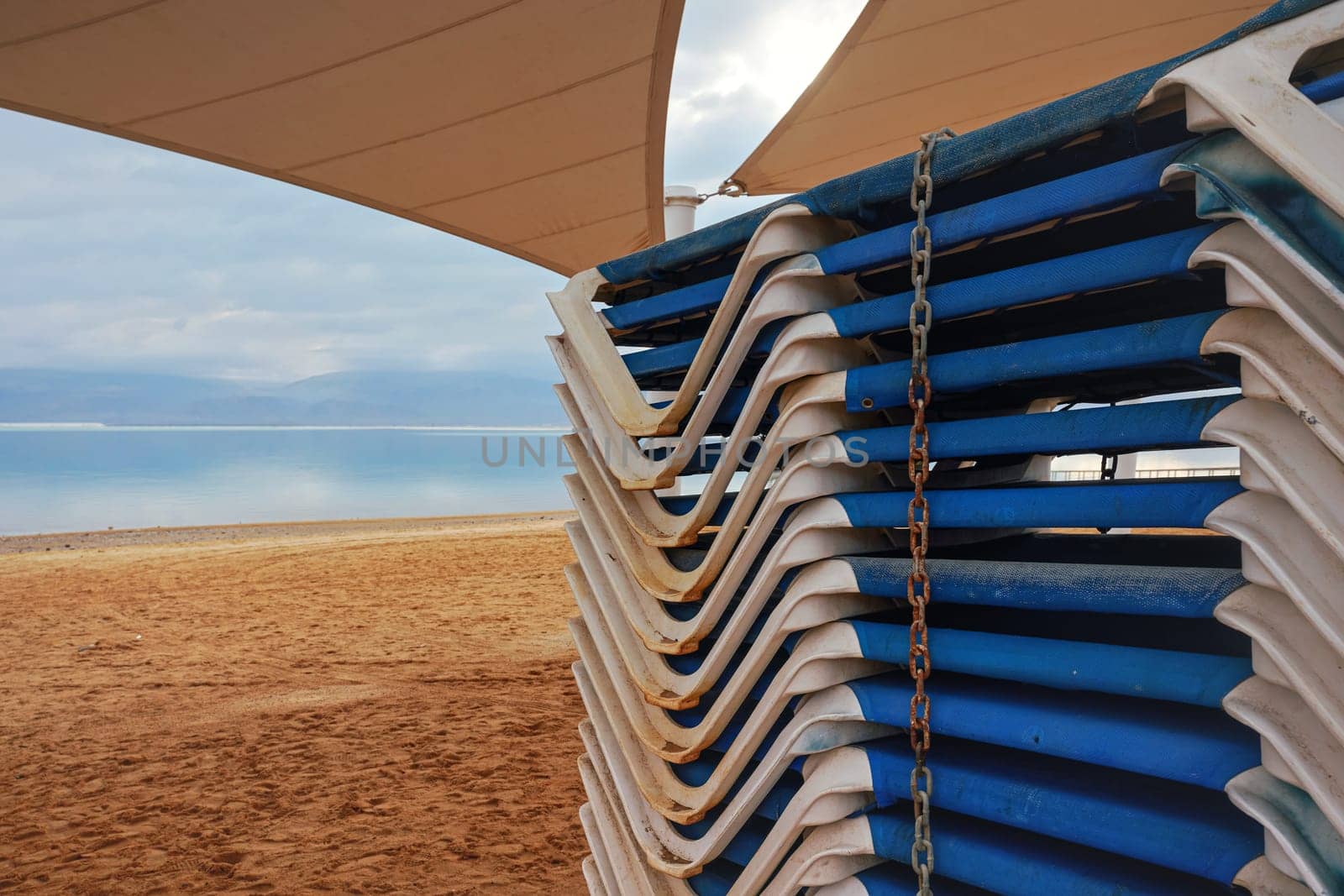Stacked plastic sun beds on the beach out of season - closeup detail, sea in distance