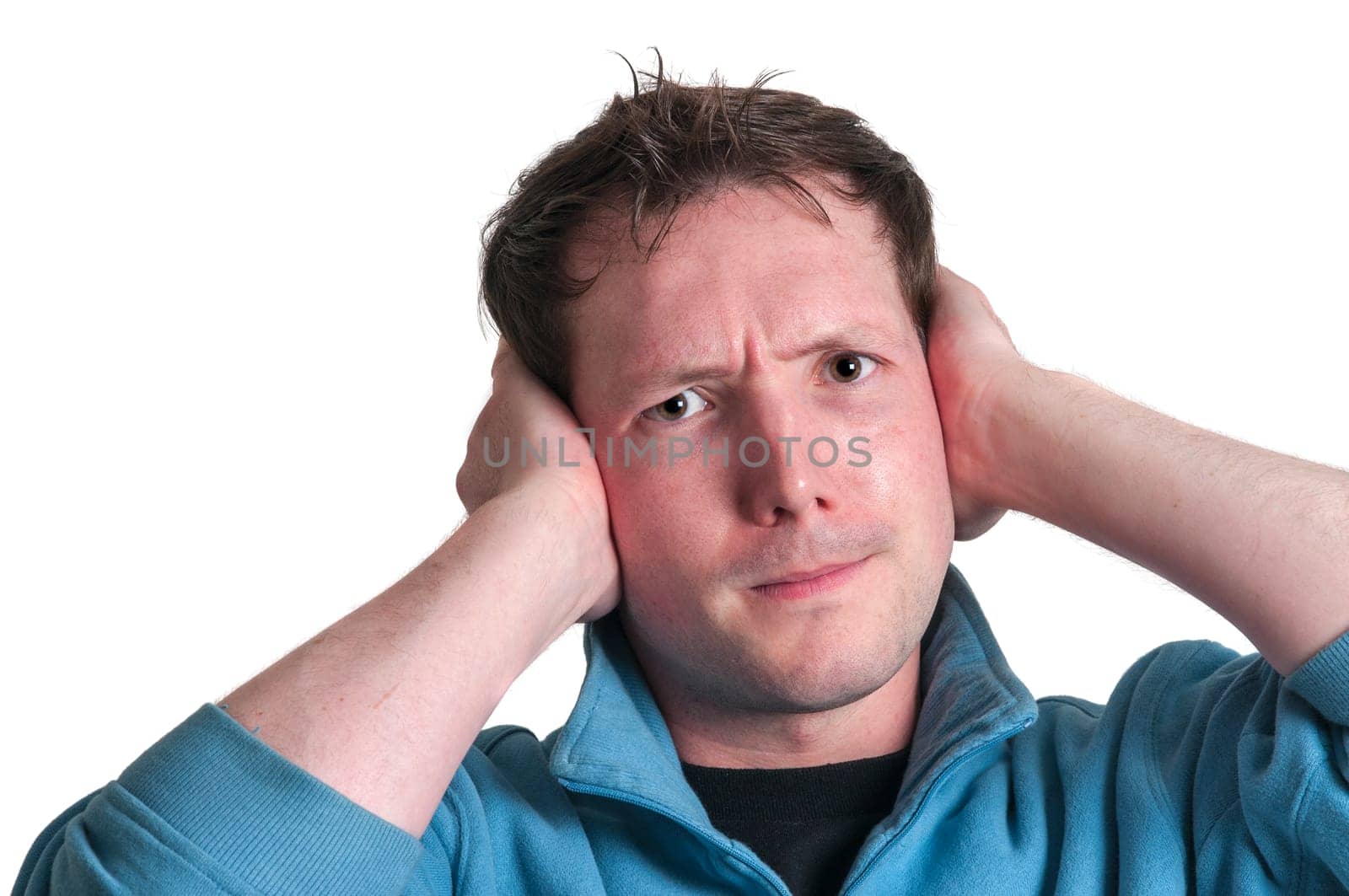 Frontal head portrait of a young brunette Caucasian man holding his hands to his ears with an annoyed facial expression and looking at the camera isolated on white.