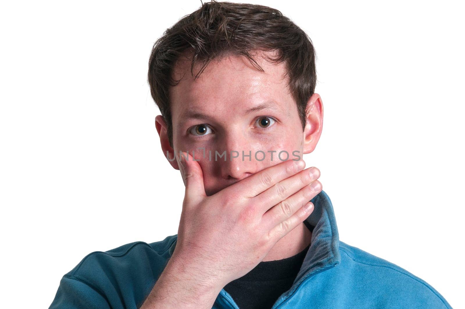 Frontal head portrait of a young brunette Caucasian man covering his mouth with his right hand and looking at the camera isolated on white.