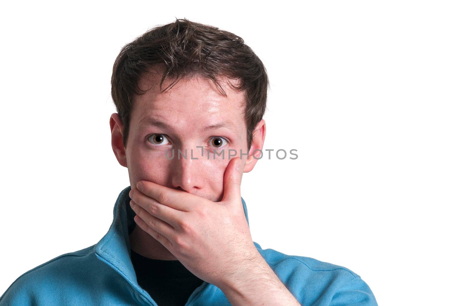 Frontal head portrait of a young brunette Caucasian man covering his mouth with his left hand while looking at the camera in shock isolated on white.
