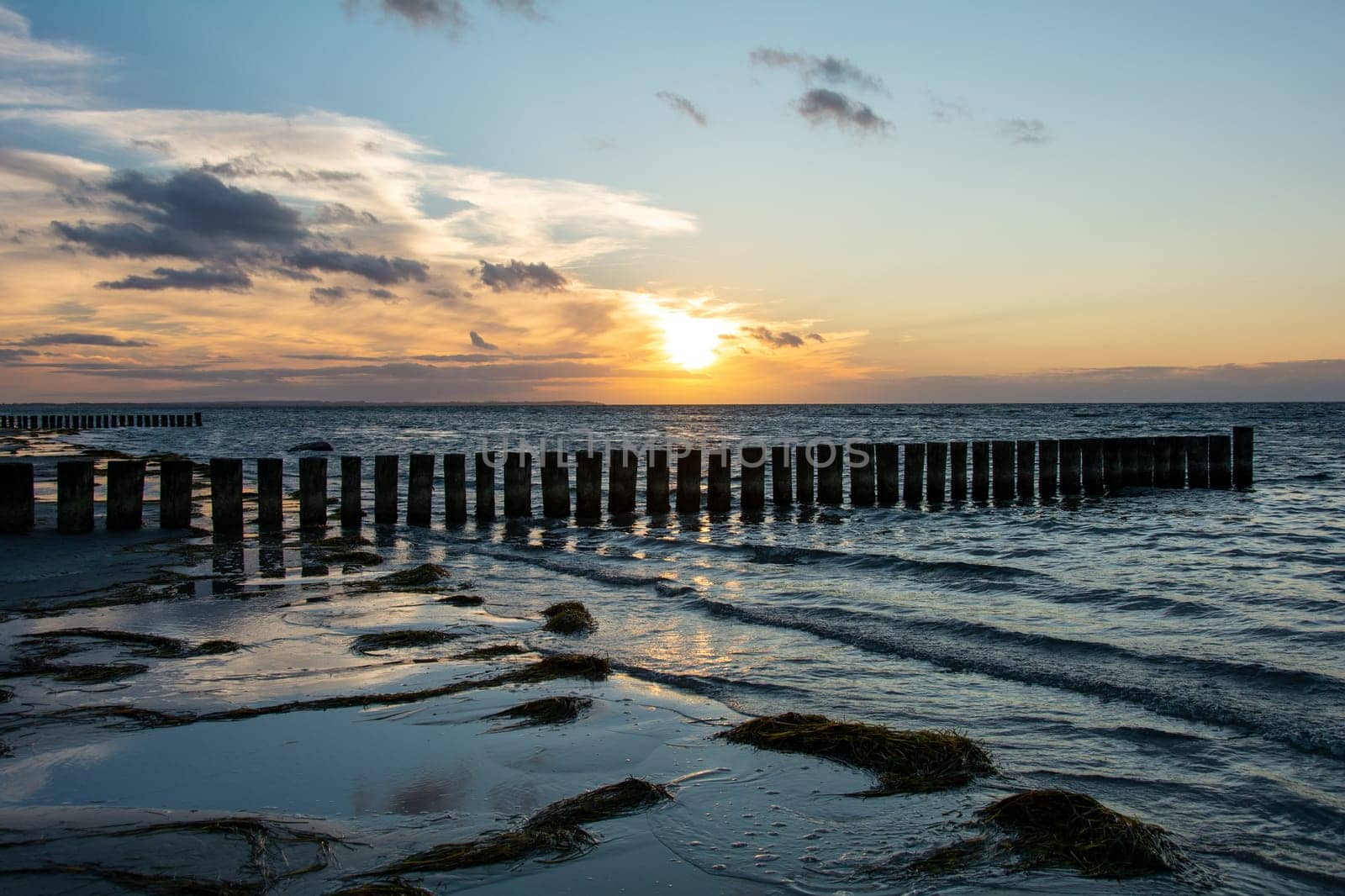 Beautiful orange sunset over the sea, with wooden breakwater in the water