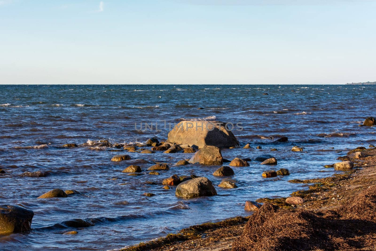 Big stones lie in the water on the Baltic Sea coast, with waves and horizon