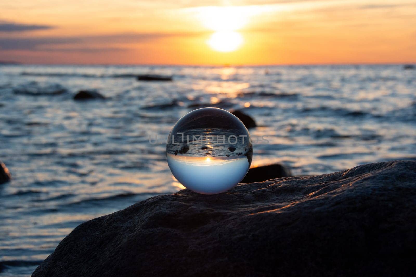 Glass ball on a rock at sunset on the beach, the sea and the setting sun are reflected in the ball