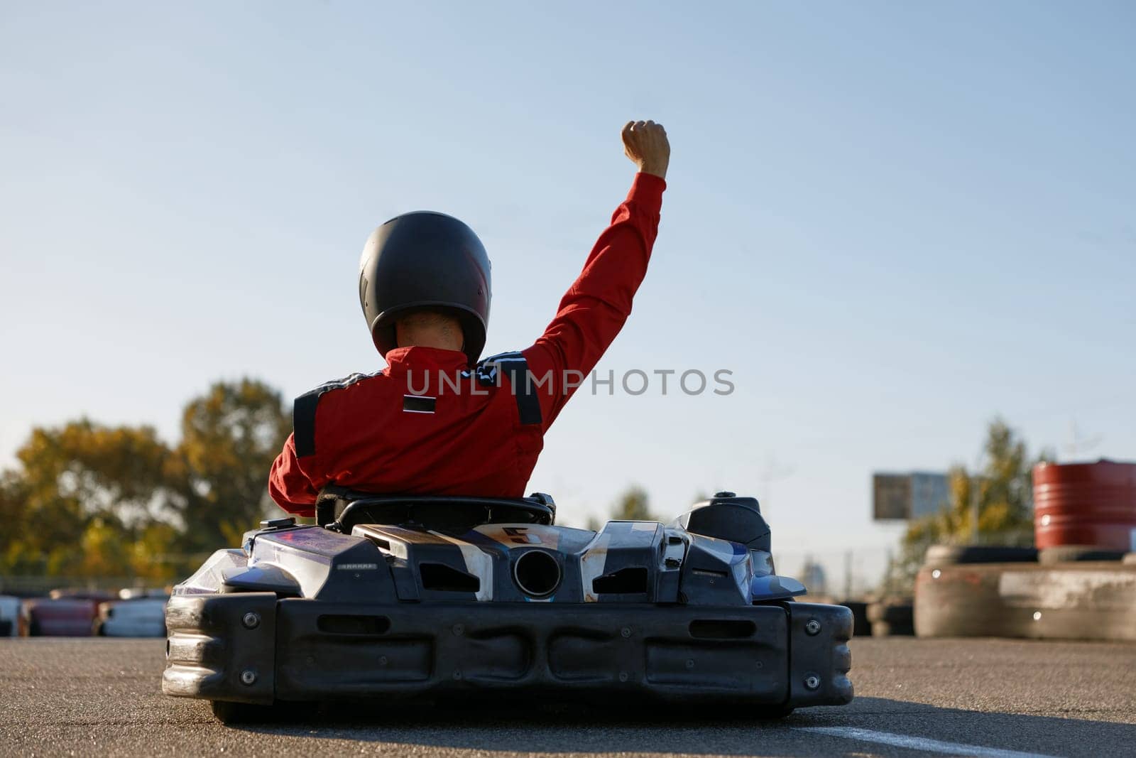 Happy go-cart driver raising hand up rejoicing and celebrating win. Carting extreme sports competition and victory in championship