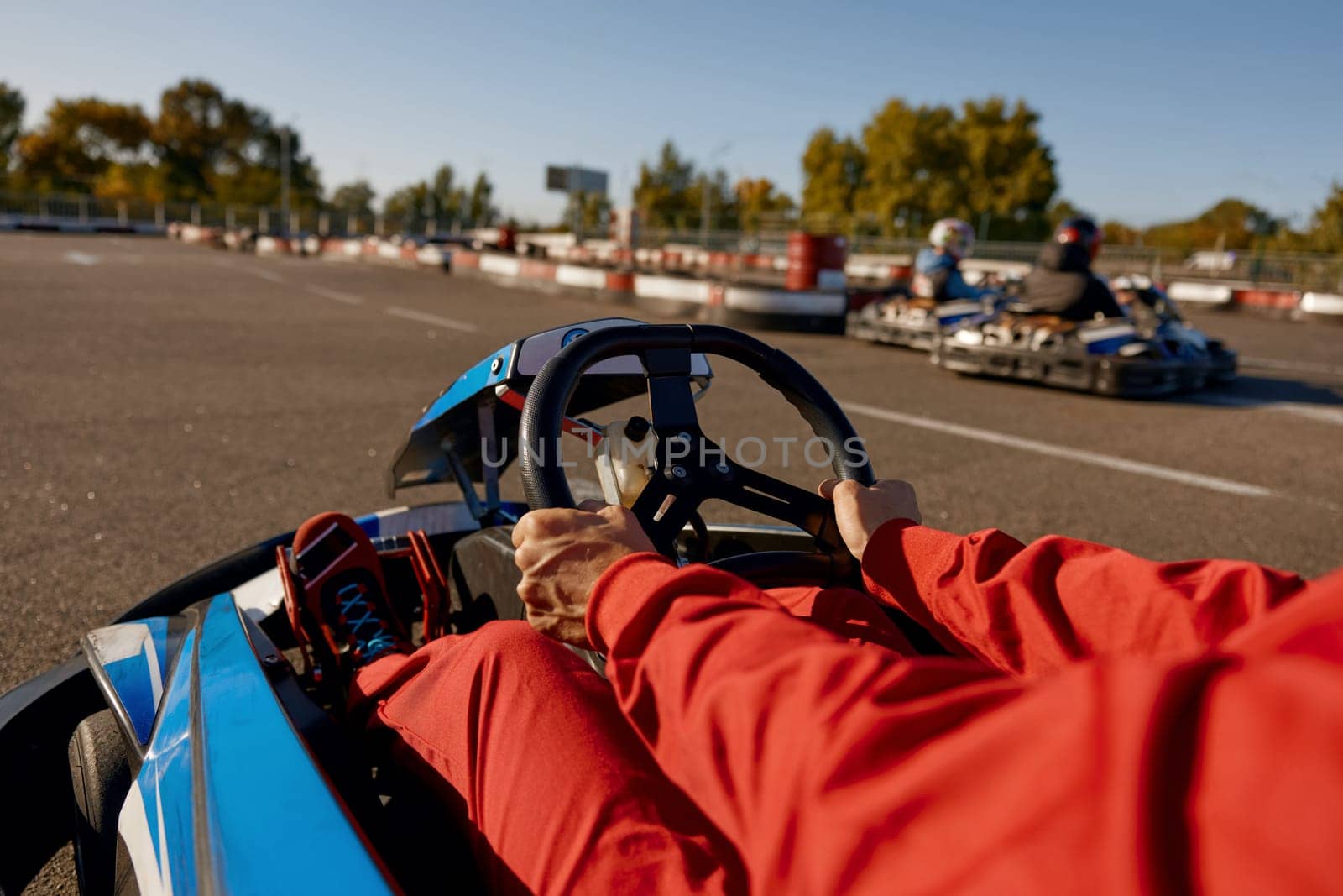 Closeup go-kart racer driving sportcar with focus on hands holding steering wheel. Recreational pursuit, carting speed racing concept