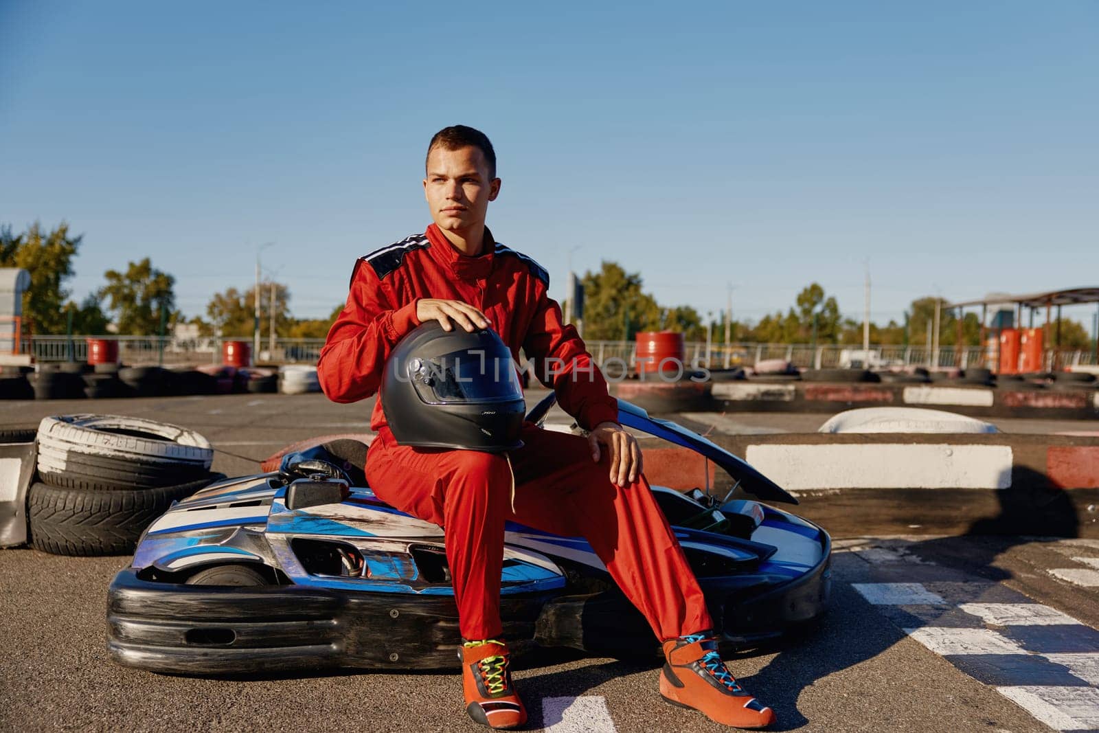 Handsome man driver with helmet sitting at his go-kart car waiting for start of competition. Professional auto sport and masculine hobby concept