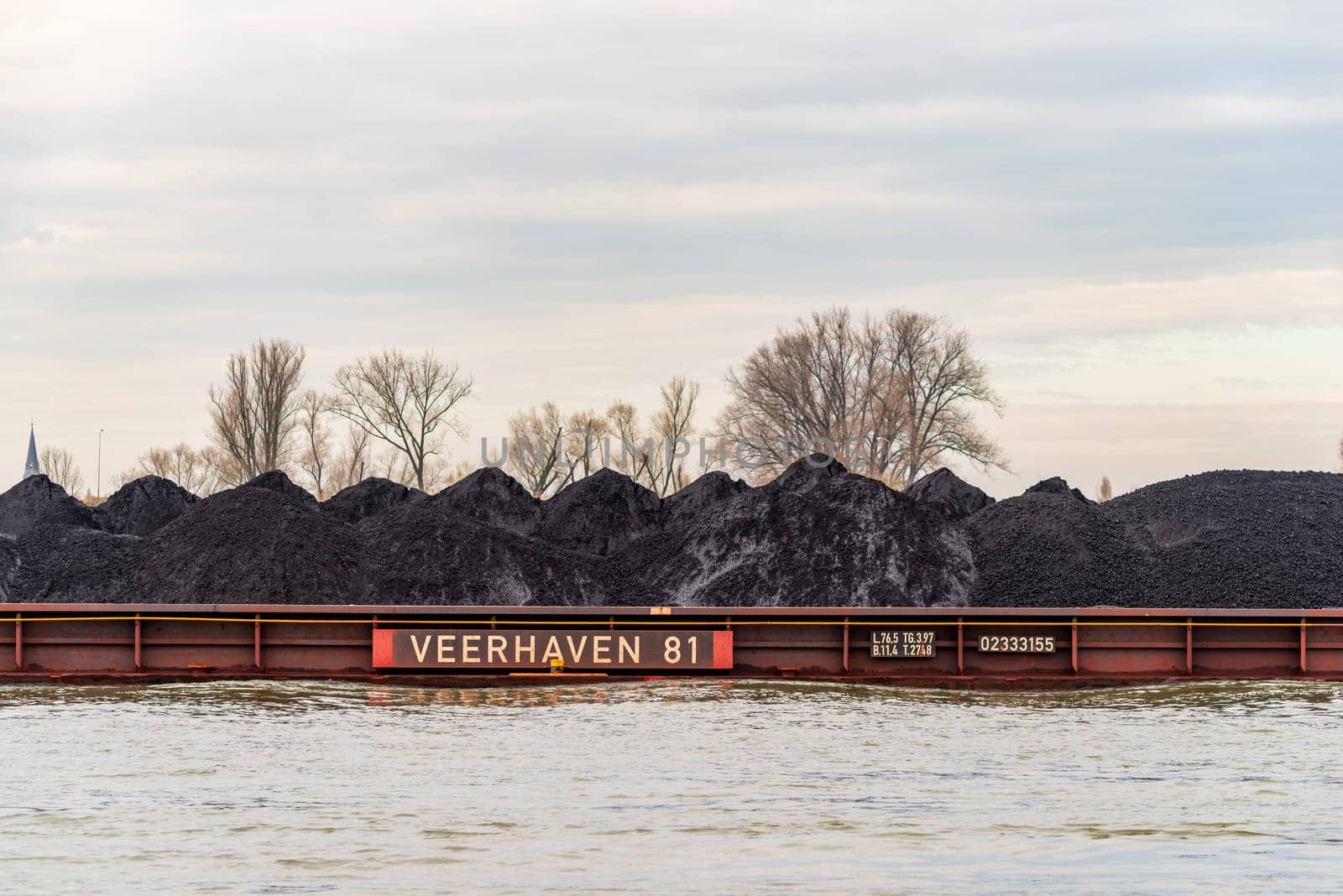 NIJMEGEN, NETHERLANDS - MARCH 9, 2024: Enormous dutch barge navigating the Waal river with a load of black sand