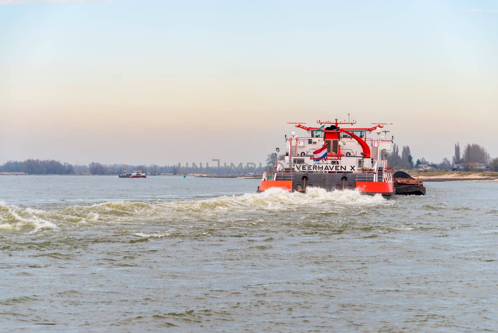 NIJMEGEN, NETHERLANDS - MARCH 9, 2024: Enormous dutch barge navigating the Waal river with a load of black sand