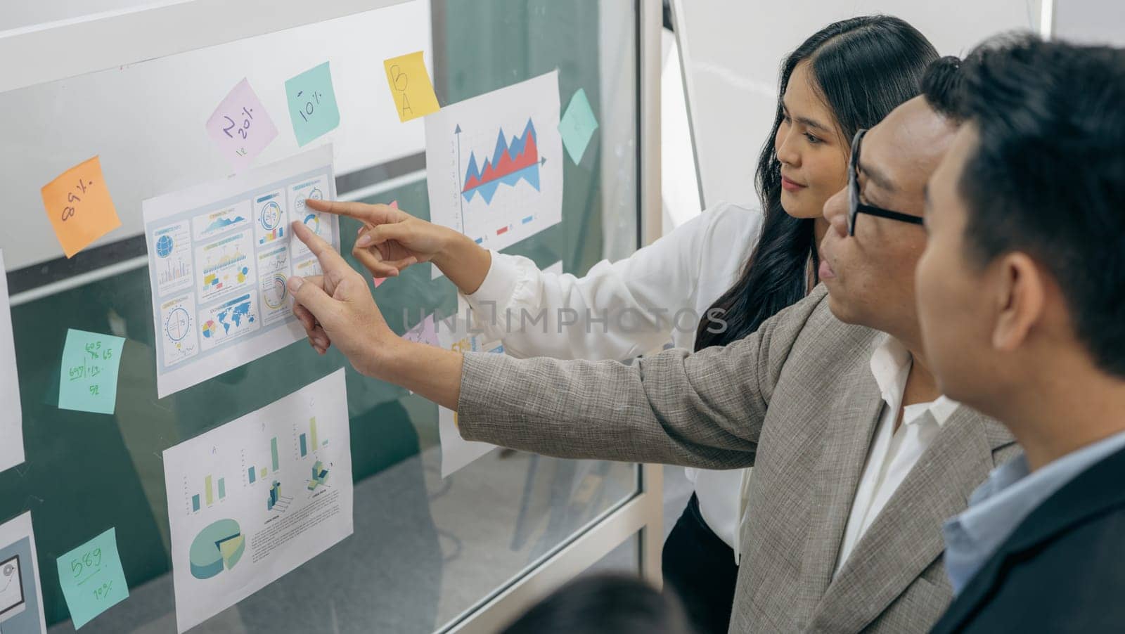A group of people are looking at a large board with graphs and charts. One of the people is pointing to a specific area on the board