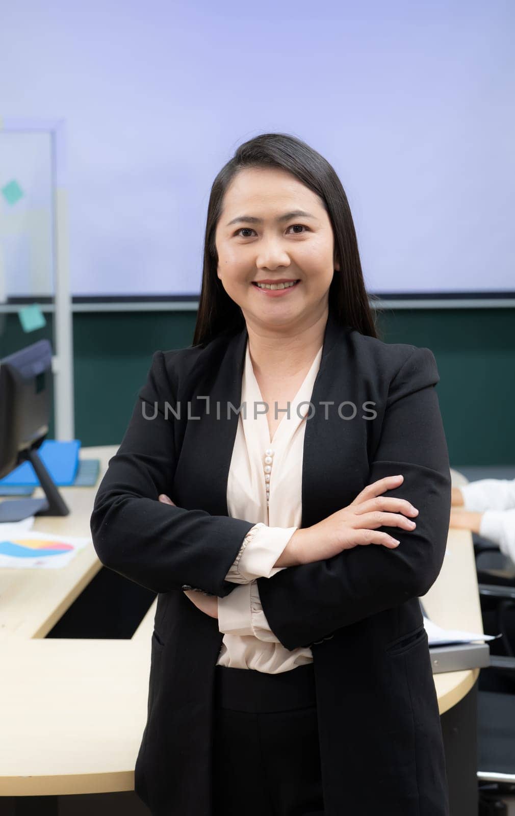 A woman in a black suit and white shirt is smiling and standing with her arms crossed. She is confident and professional