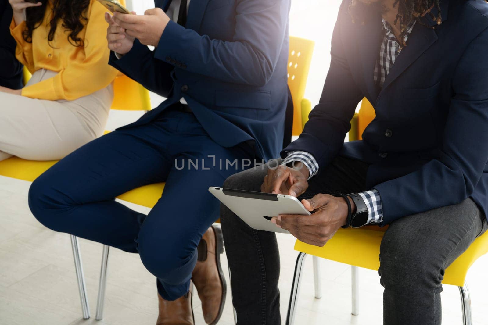 Two men in suits are sitting in chairs, one of them holding a tablet. Concept of professionalism and focus, as the men are likely engaged in a work-related activity. The use of technology
