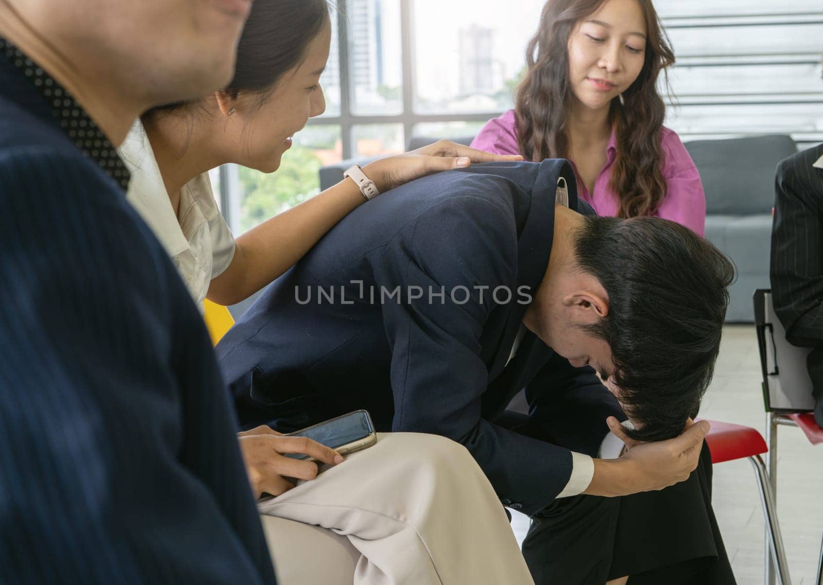 A man is crying while a woman comforts him. The other people in the room are watching