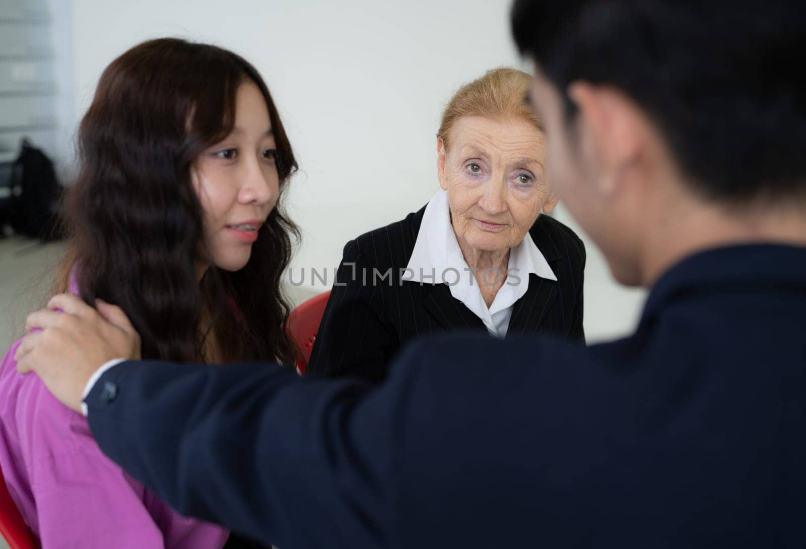 A woman in a black shirt and white shirt is sitting in a chair with two other people