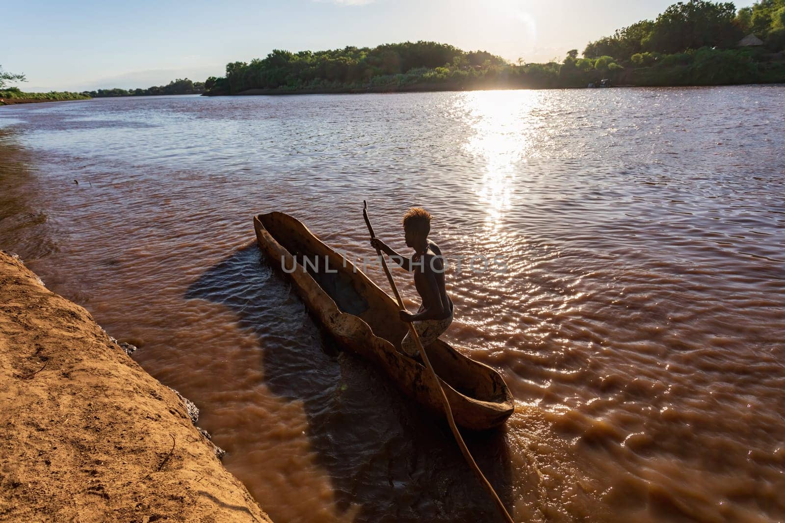 Silhouette of a Ferryman man paddling on a traditional coarse wooden boat, crossing the river Omo, Omo valley, Omorati Etiopia