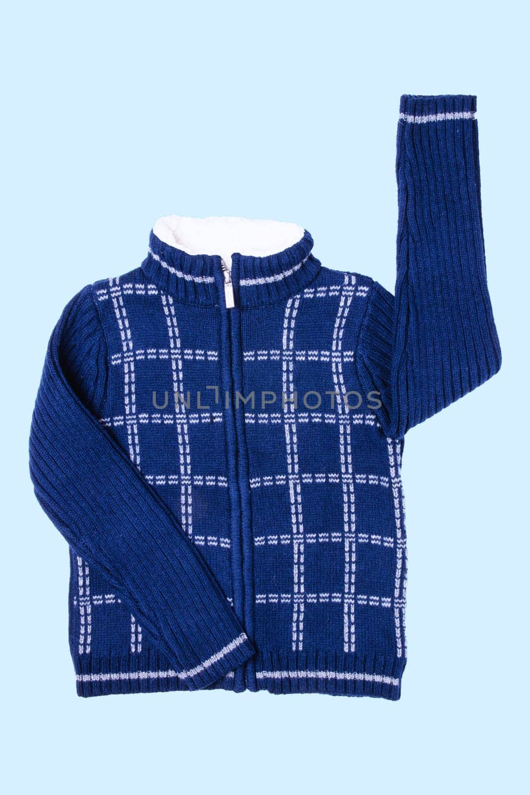 Autumn and winter jacket. A dark blue woolen knitted cardigan or pullover with a white checkered pattern on light blue background. Kids cozy warm jumper or  sweater fashion.