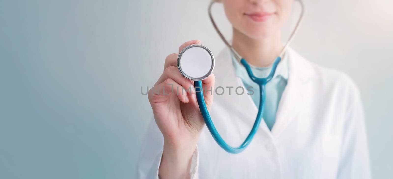 Closeup woman doctor holding a stethoscope listening the pacient stretching her hand to the screen. Medical worker on light blue background with copy space