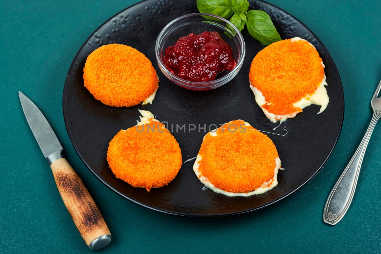 Fried camembert or brie cheese with berry jam and basil. Cheese baked in the oven.