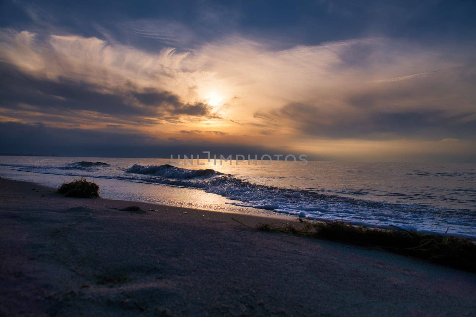 Sunset, illuminated sea. Sandy beach in the foreground. Light waves. Baltic Sea. Landscape on the coast