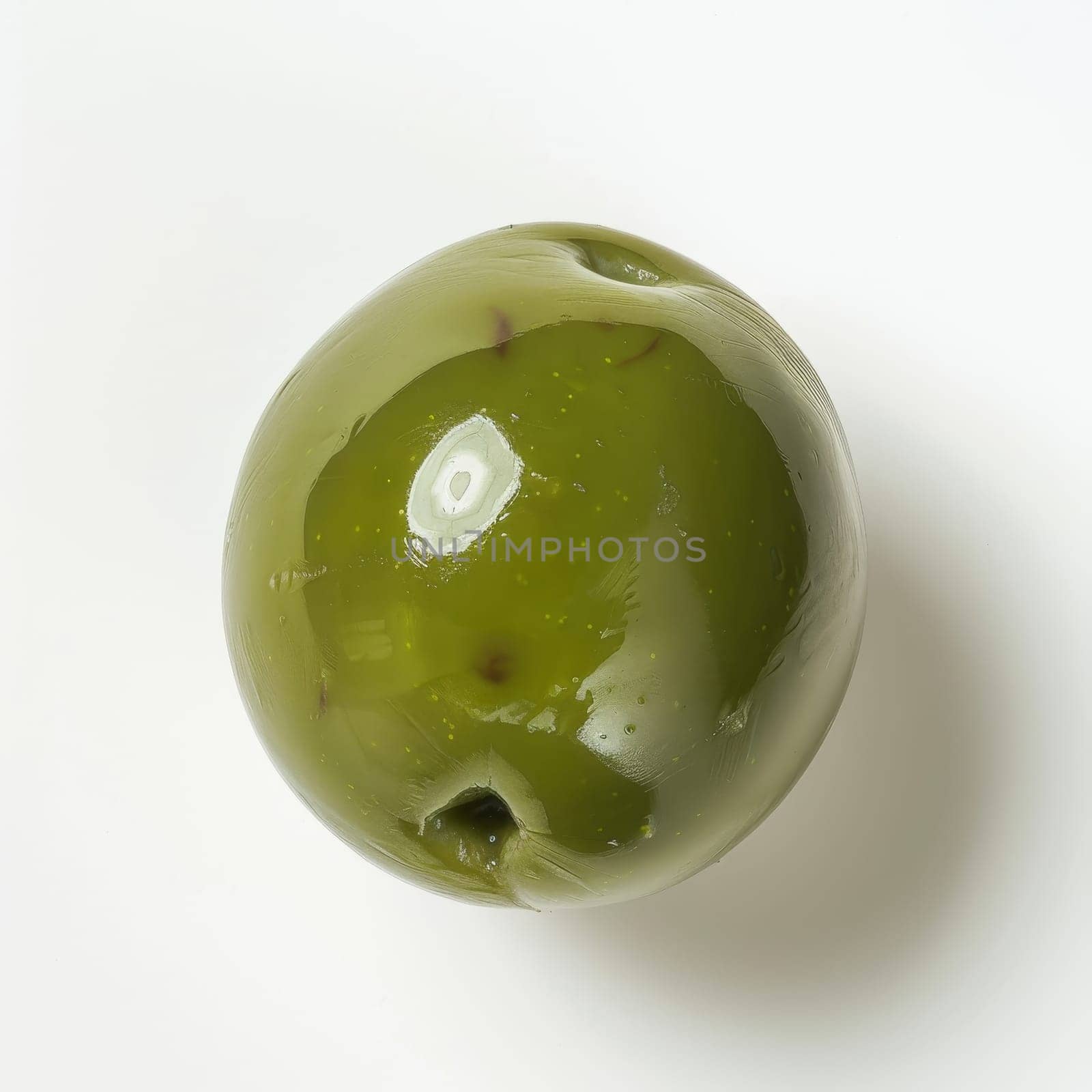 A single green olive sits on a white background. The olive is smooth and slightly wrinkled, with a small stem attached