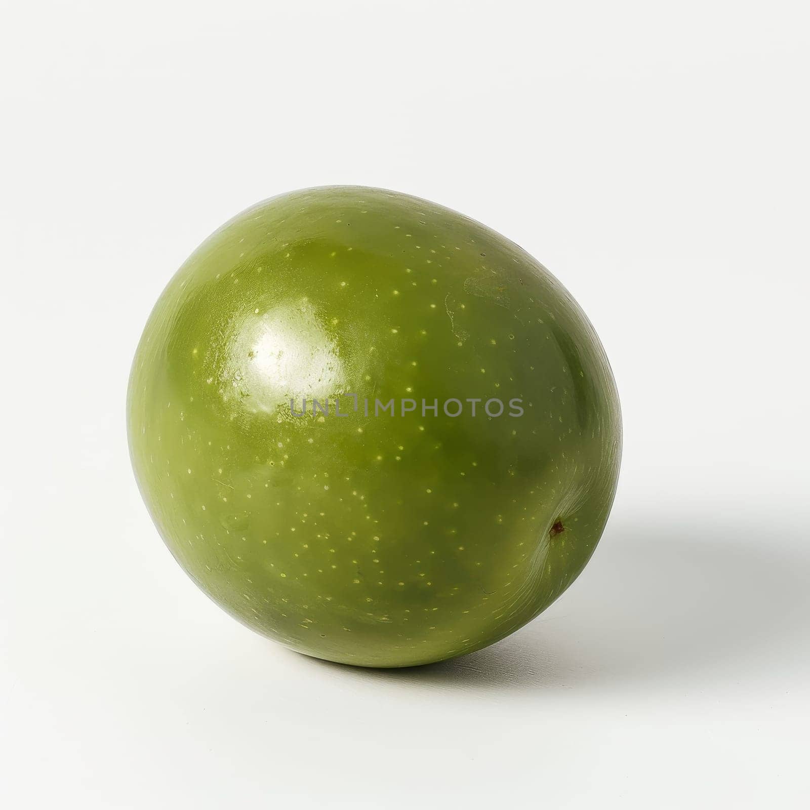 A single green olive sits on a white background. The olive is smooth and slightly wrinkled, with a small stem attached