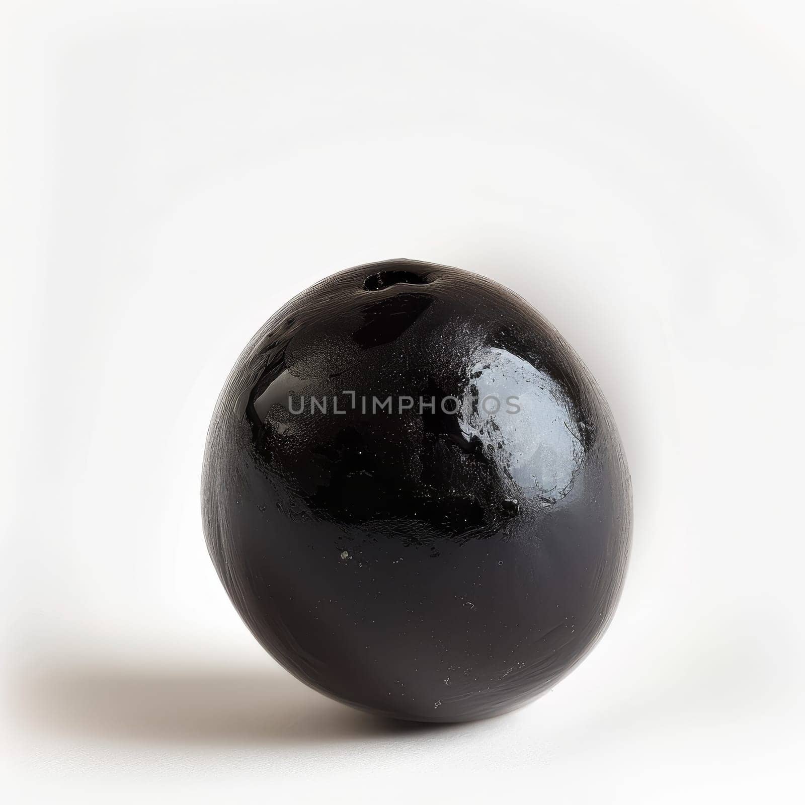 A ripe, glossy black olive with water droplets, isolated on a white background
