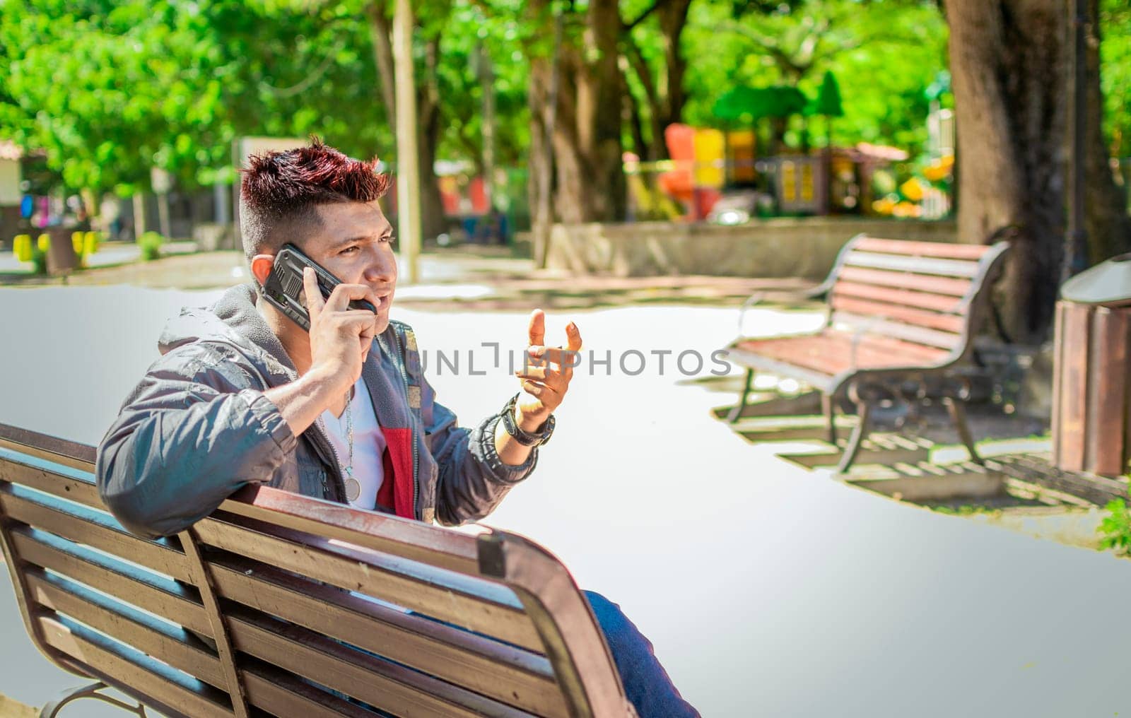 Man sitting on a bench calling on the phone, young man sitting on a bench with cell phone, close up of a young man calling on the phone sitting on a bench