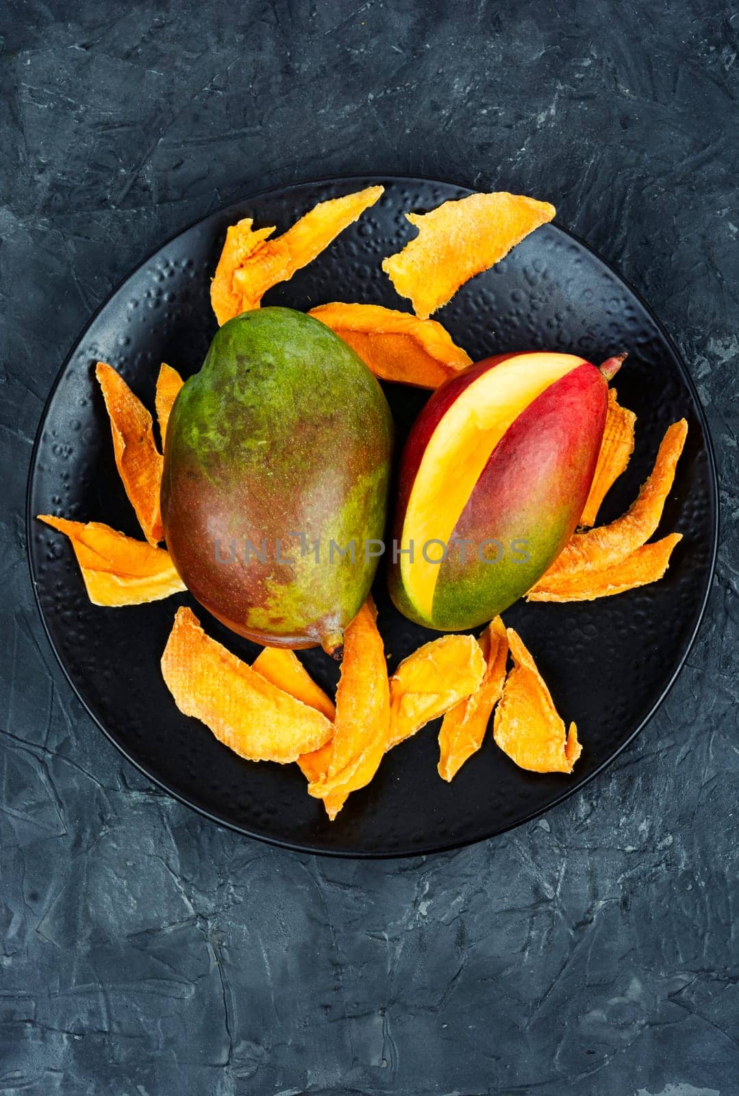 Dried mango pieces with knife and raw fruits. Top view.