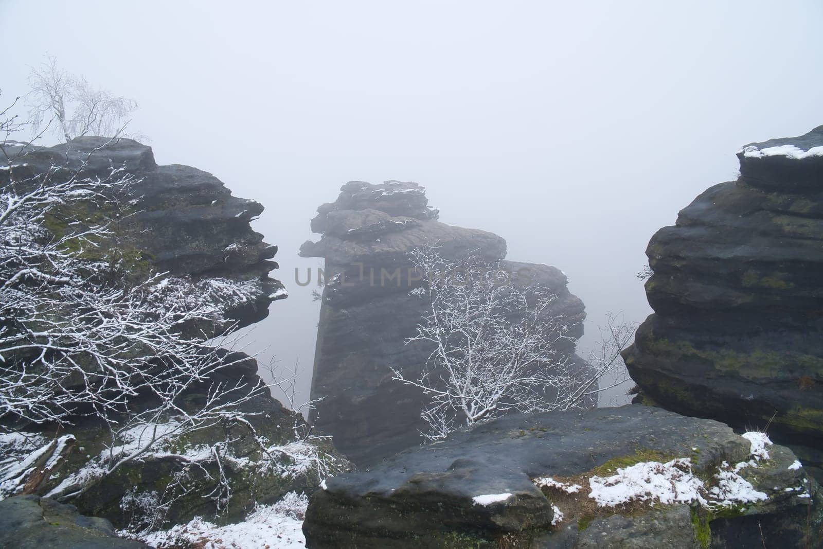 On the large Zschirnstein in fog. Rock covered with snow. Viewpoint during a hike. From the nature park in the Elbe Sandstone Mountains. Landscape in Germany