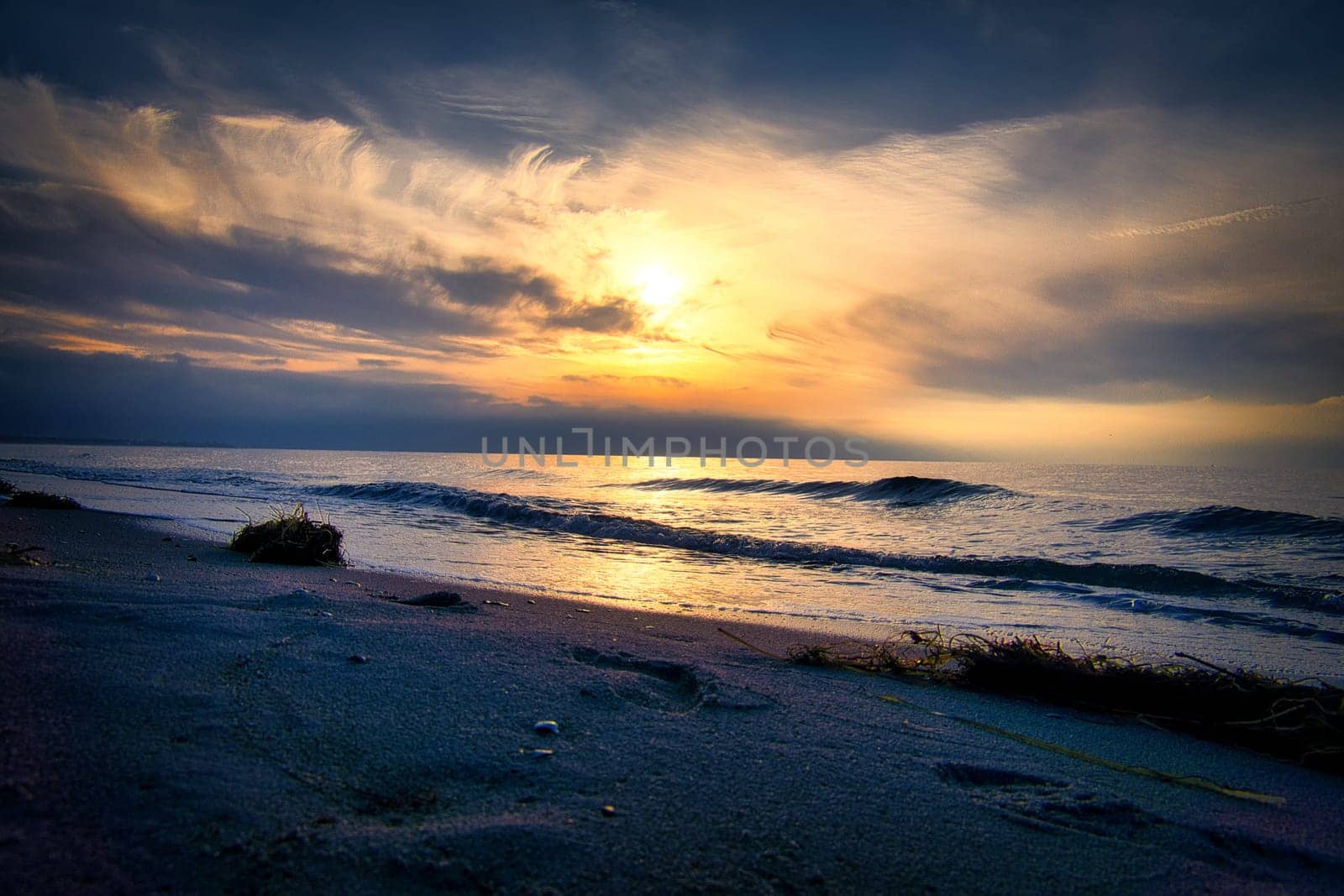 Sunset, illuminated sea. Sandy beach in the foreground. Light waves. Baltic Sea. Landscape on the coast