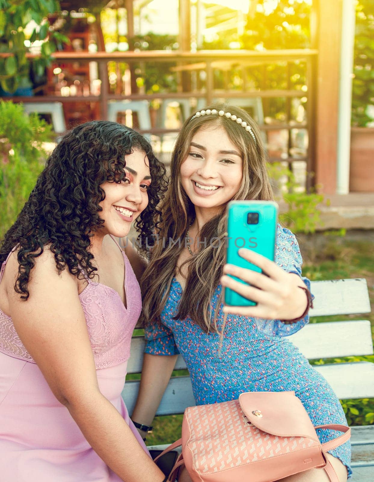 Two pretty girls sitting on a bench taking a selfie, girls smiling and taking a selfie, sisterly friendship concept