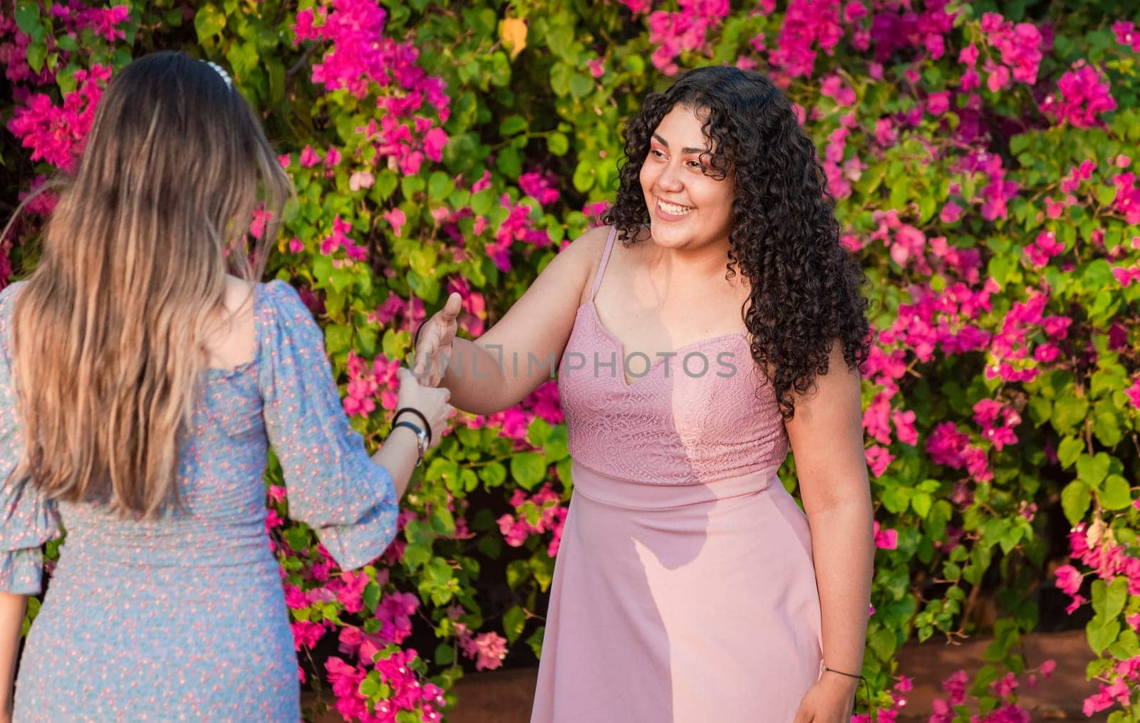 Two girls friends waving and shaking hands, two smiling girls shaking hands on the street