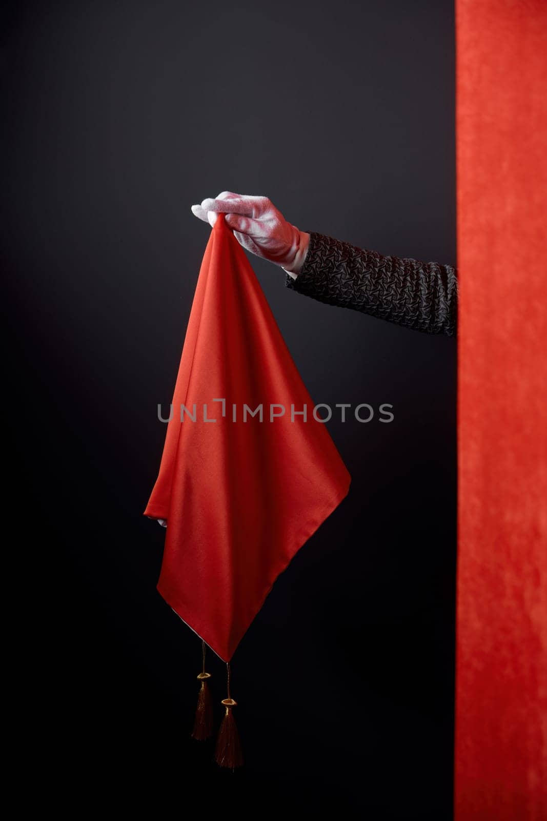 Talent show performance, illusionist entertaining magical trick concept. Closeup hiding magician hand behind red drapery holding magic handkerchief