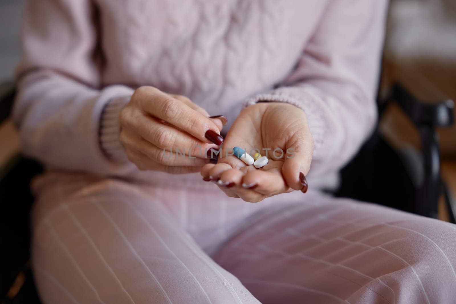 Closeup of old woman in wheelchair taking prescribed pills for rehabilitation and healthcare at hospice