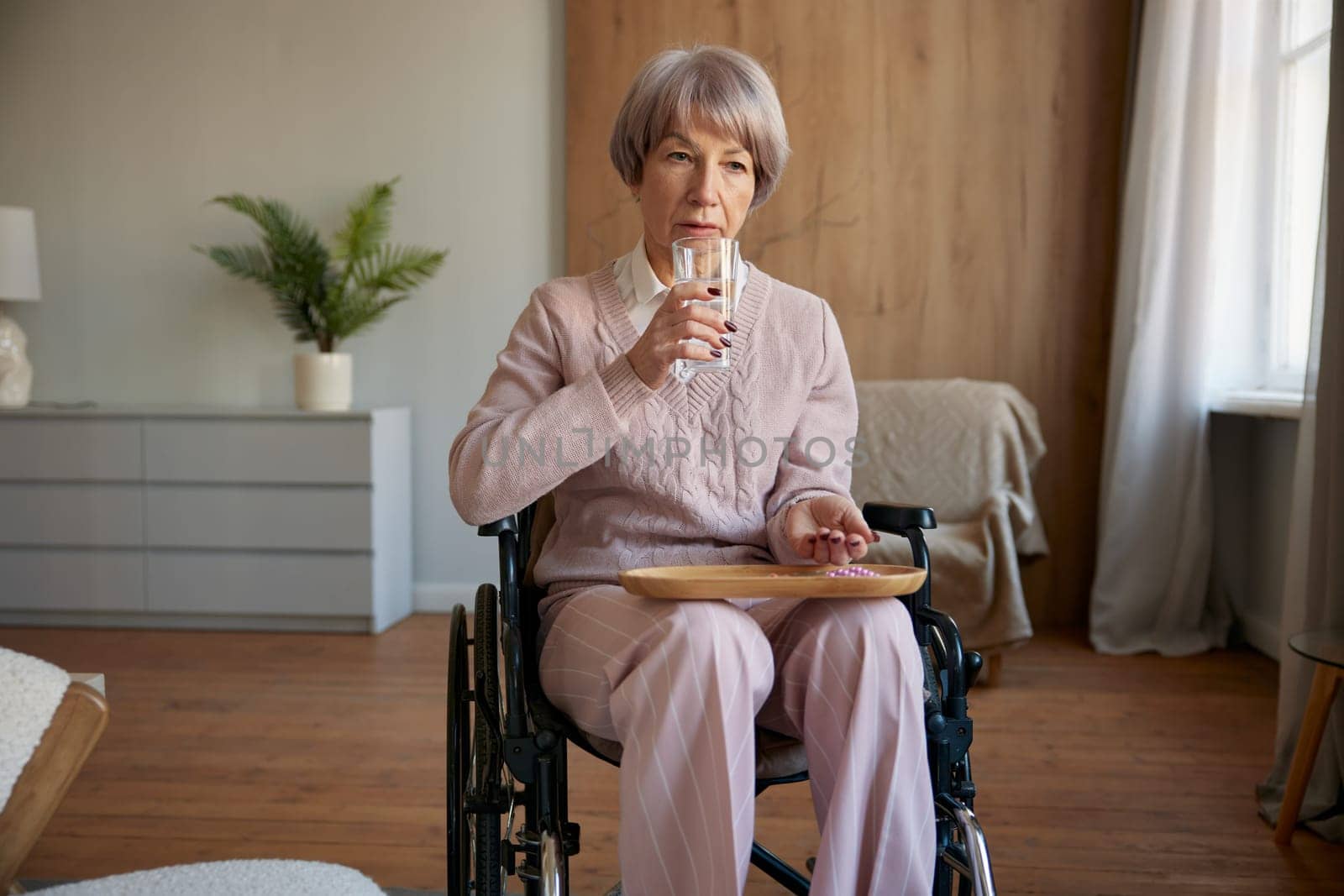 Lonely sad old woman in wheelchair taking prescribed pills for rehabilitation and healthcare at hospice