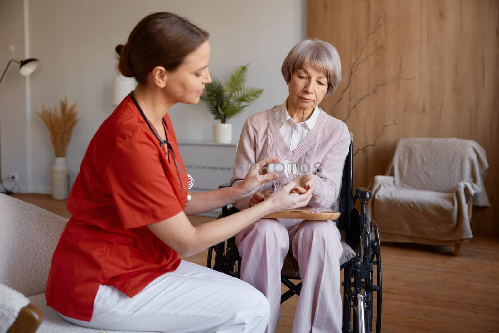 Woman nurse caregiver giving pills to old woman for healthcare support. Medical help and retirement health insurance for elderly people at nursing home concept