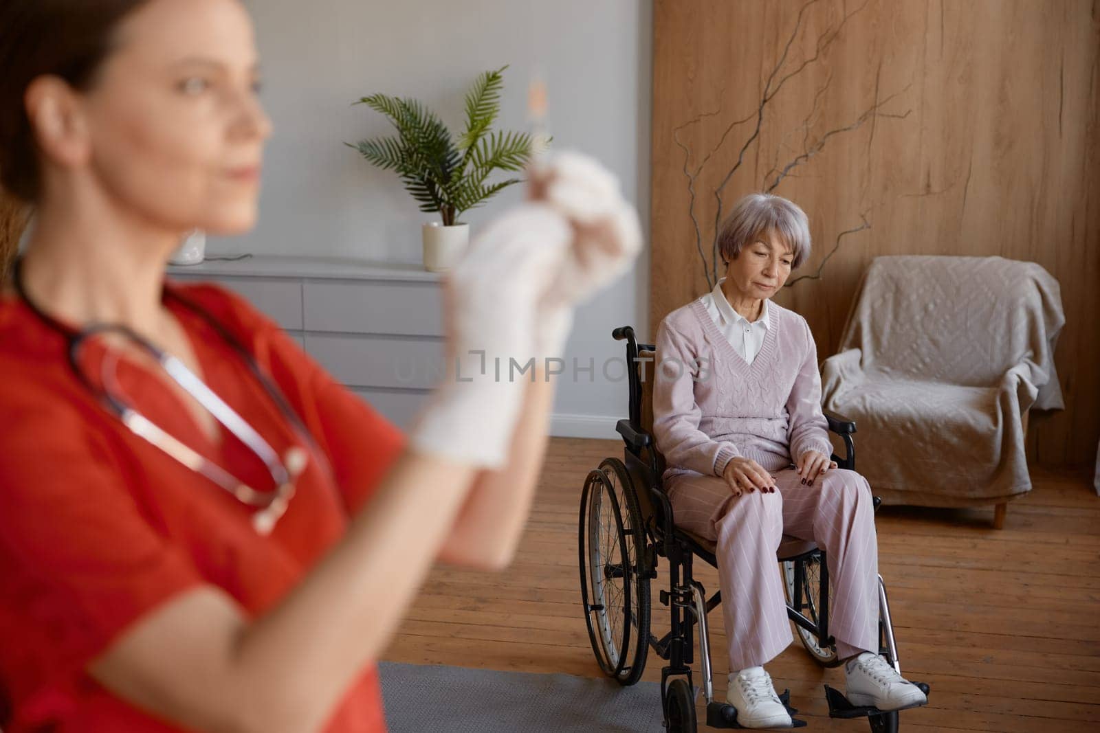 Qualified professional woman nurse preparing syringe for vaccination of old lady patient at retirement house. Medicinal injection for elderly people during corona or flu outbreak