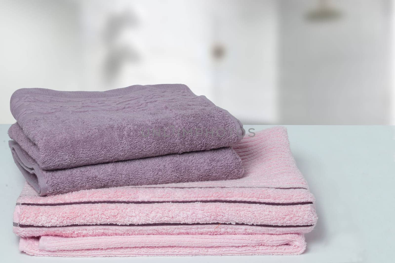 Table top on towels background. Closeup of a stack or pile of violet and pink soft terry bath towels at a bright table against blurred bathroom background. Space.