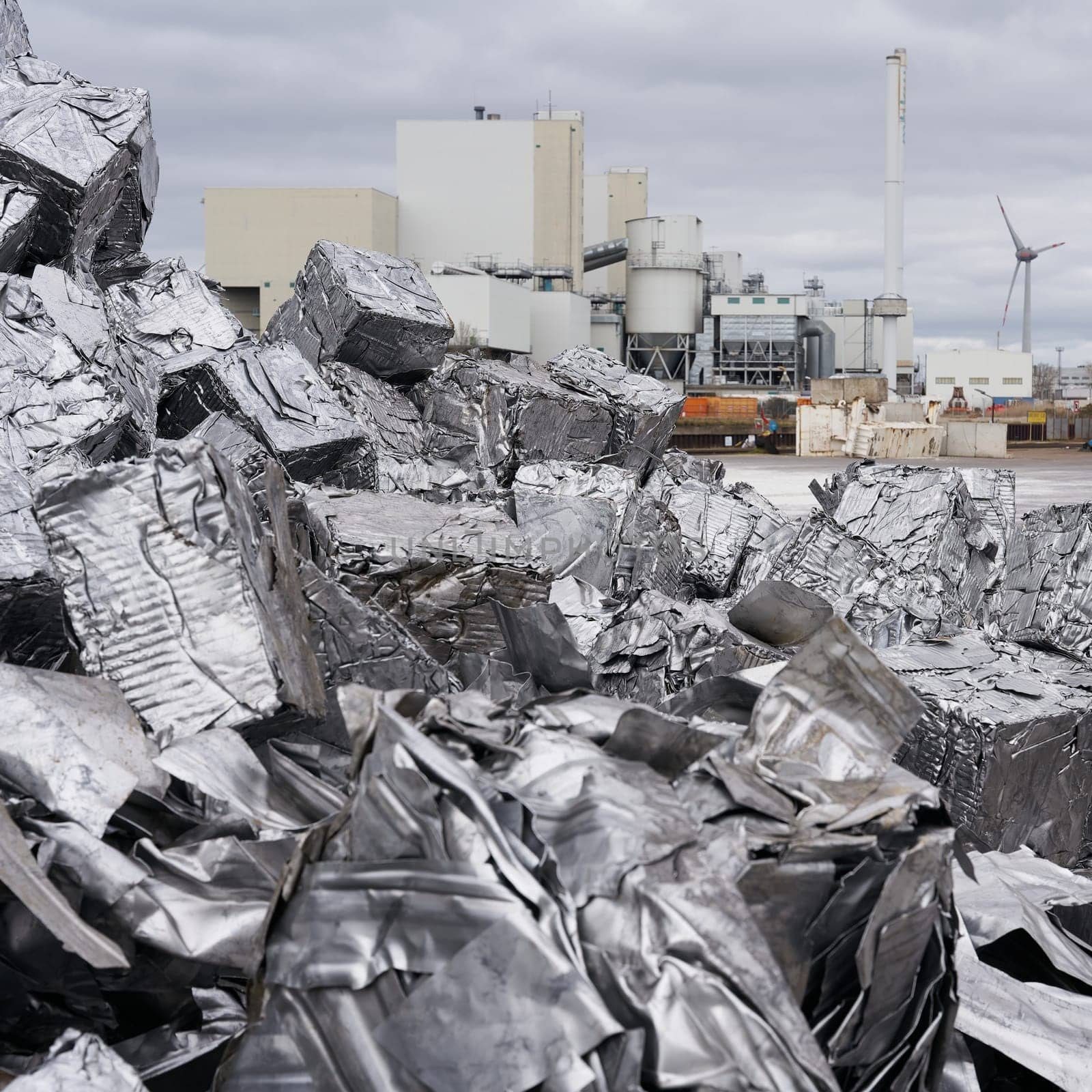 Pressed scrap metal at a scrap yard in the port of Magdeburg in Germany, a factory in the background
