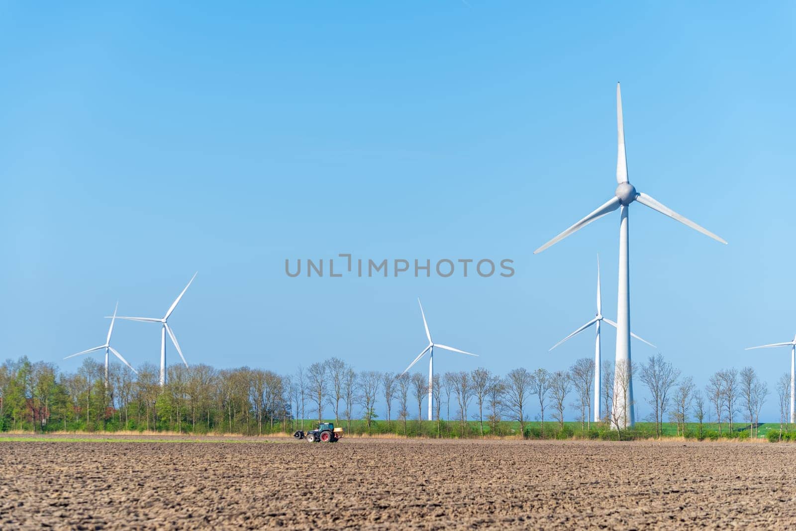 enormous wind turbines with a tractor in the foreground plowing his land