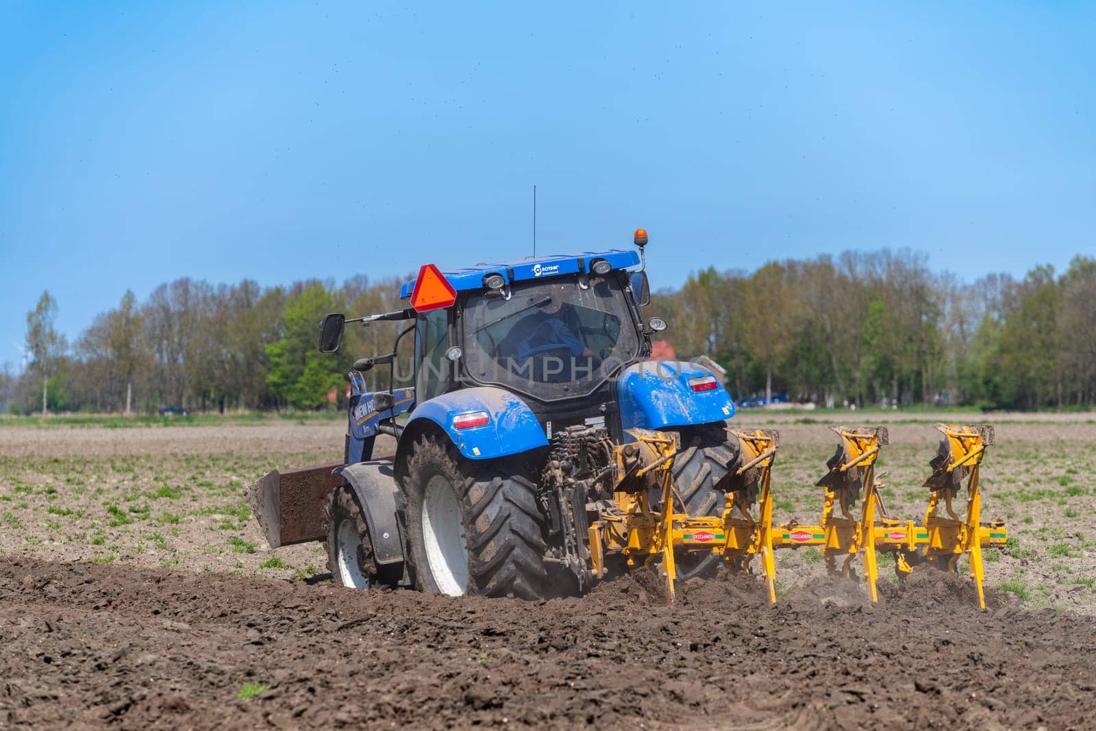 EMMELOORD, NETHERLANDS - APRIL 21, 2018: Farmer with his tractor plowing his land in early spring