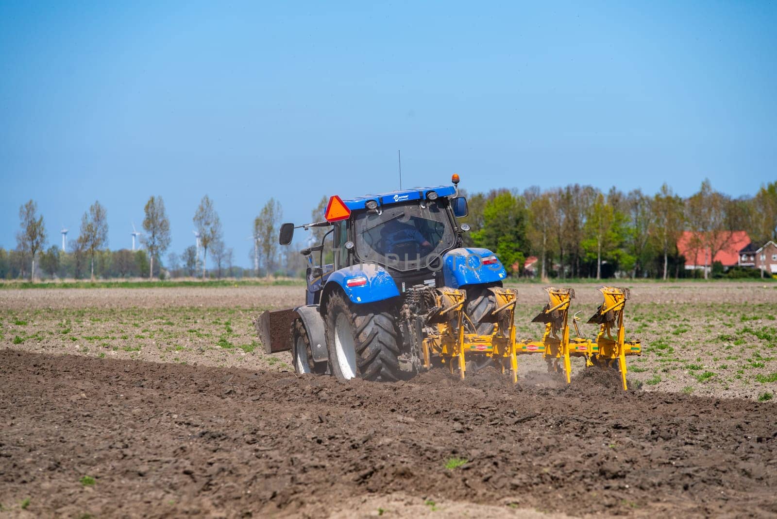 EMMELOORD, NETHERLANDS - APRIL 21, 2018: Farmer with his tractor plowing his land in early spring