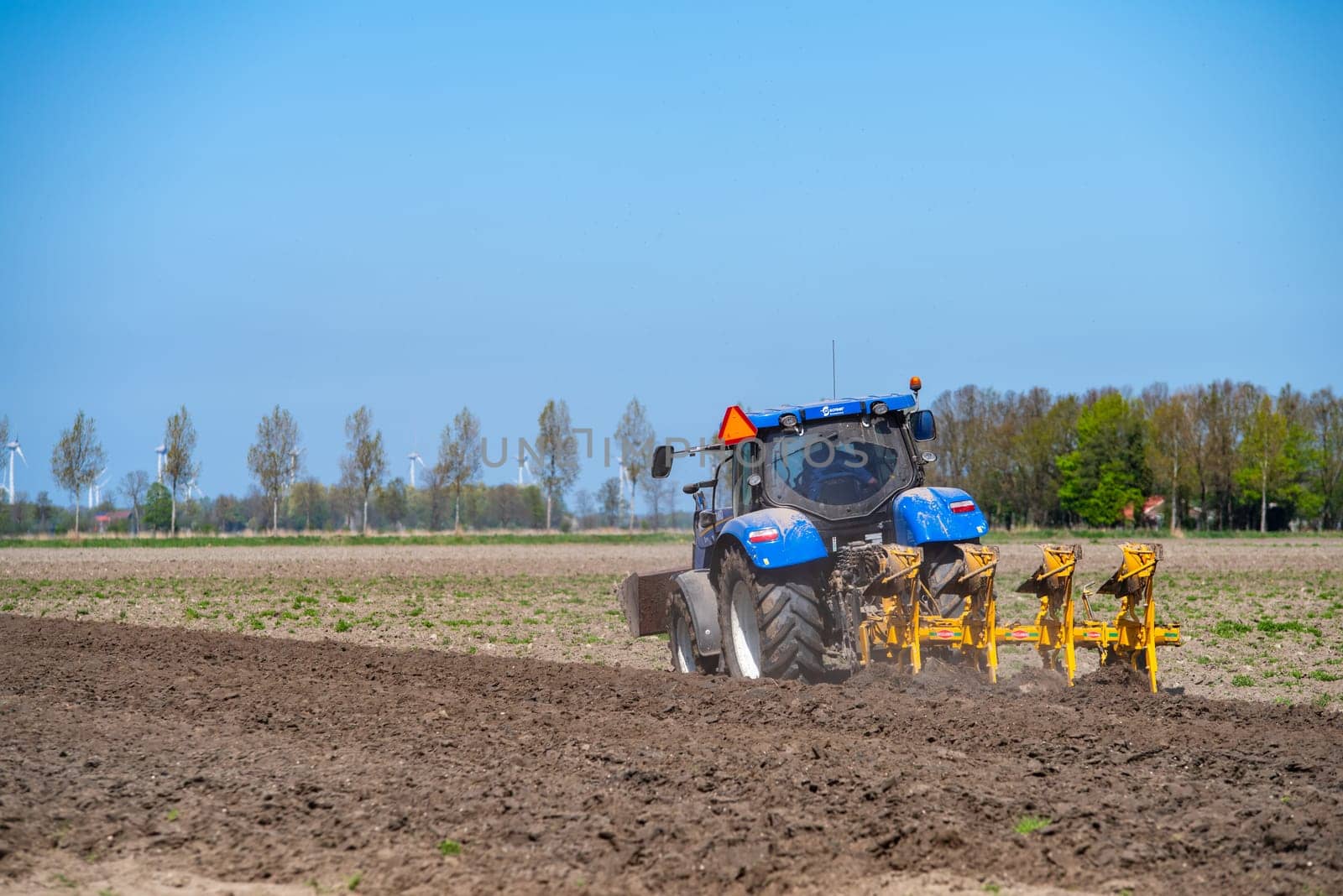 EMMELOORD, NETHERLANDS - APRIL 21, 2018: Farmer with his tractor plowing his land in early spring