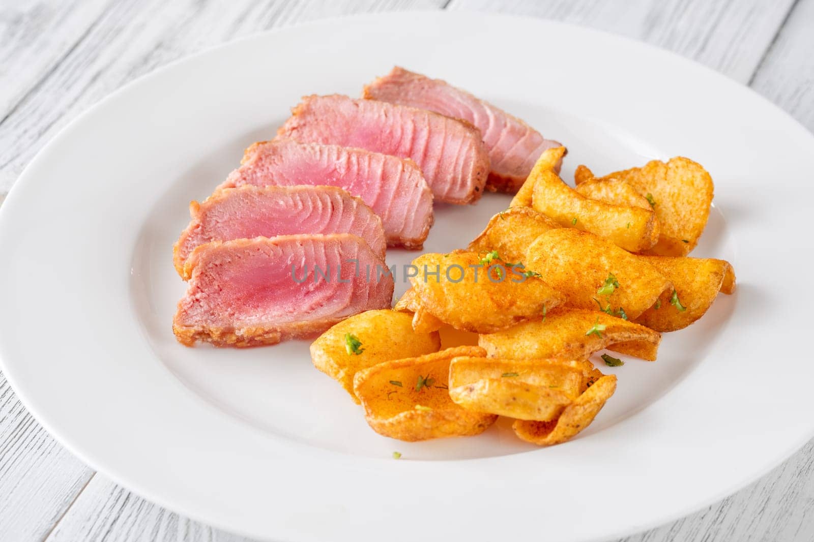 Portion of tuna with potato dippers on the plate