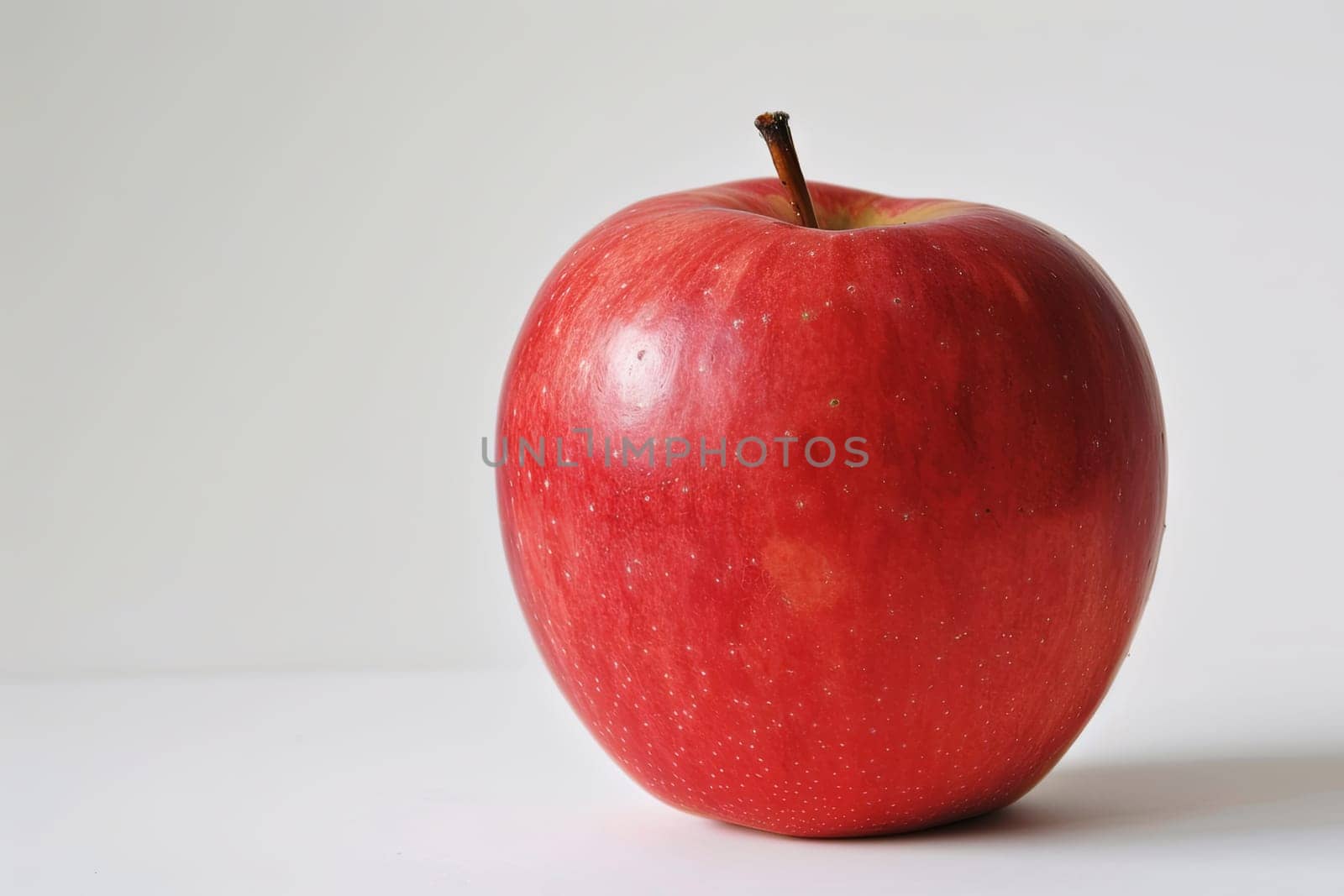A single ripe red apple is placed meticulously on top of a clean white table surface. The contrast between the bright red fruit and the stark white table creates a visually striking scene in this simple yet elegant composition.