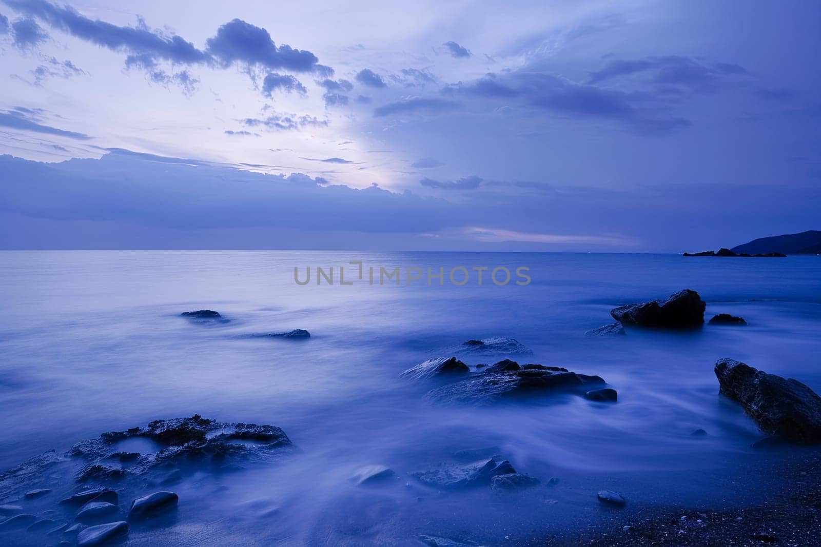 Waves crash against rocks in the foreground as the ocean stretches into the distance, captured in a long exposure shot.