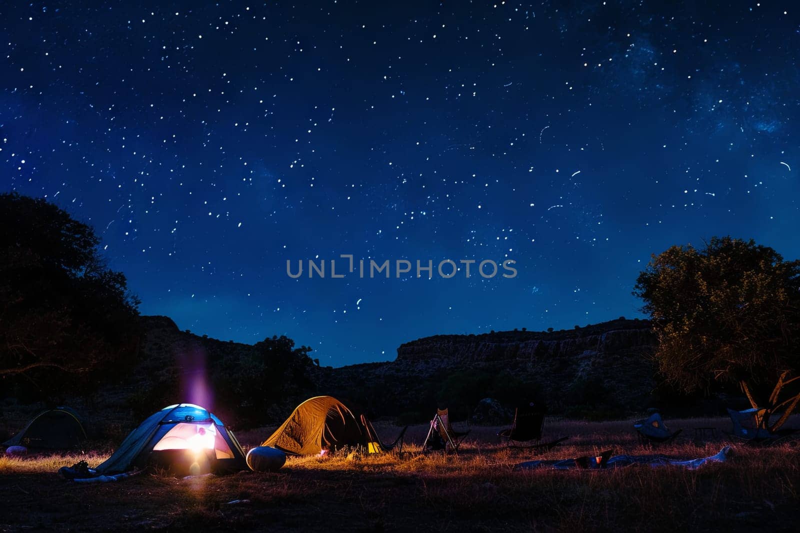 Two tents are set up on top of a vast field, illuminated by the stars in the night sky. The tents appear small against the vastness of the field and the darkness of the night.