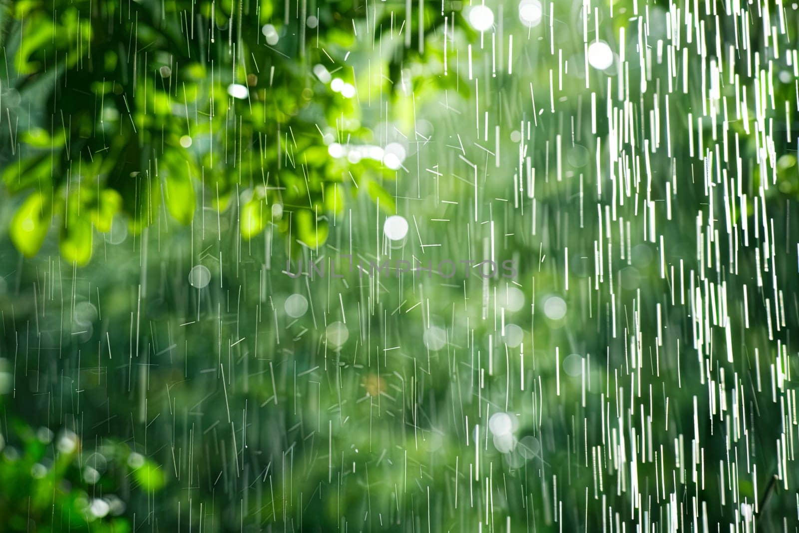 The close-up shows a rain shower head spraying water droplets with force. The metal shower head is attached to a wall, with the droplets splashing downwards.