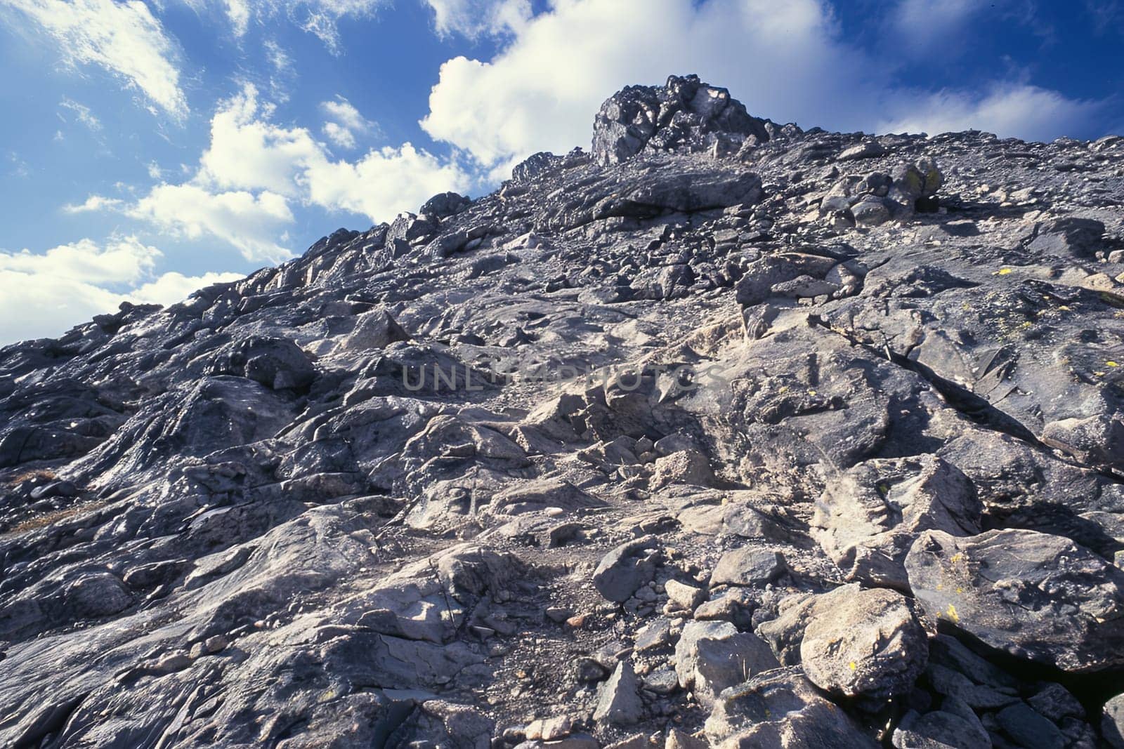 A rocky mountain dominating the scene with various sizes of rocks scattered around it. The sky serves as a backdrop, adding contrast to the rugged terrain.