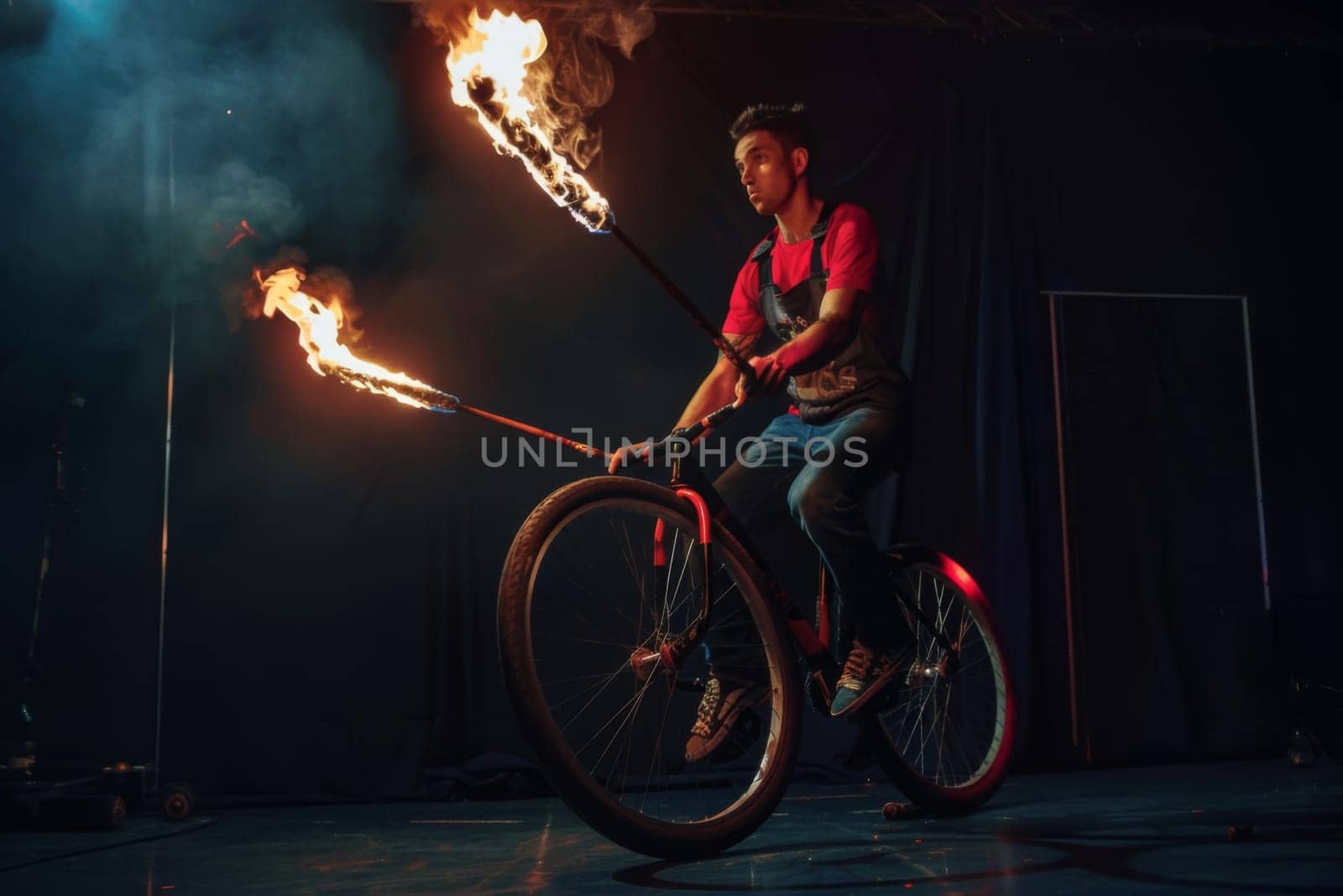 A man, riding a bike, with flames shooting up into the sky behind him.