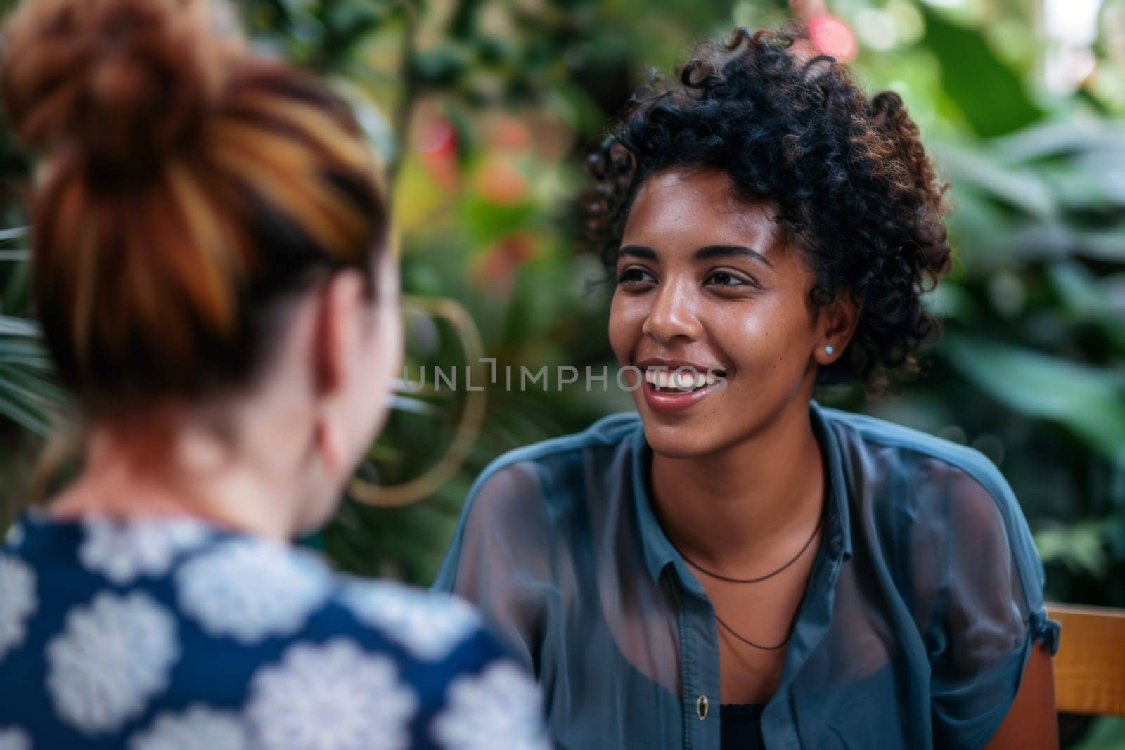 In the image, two women are seated at a table engaged in conversation. They appear to be focused on each other, possibly discussing a topic of interest. Both women seem attentive and animated in their interaction.